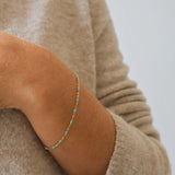 Close-up of a hand wearing a delicate 14k Gold Turquoise Beaded Bracelet on a beige sweater.