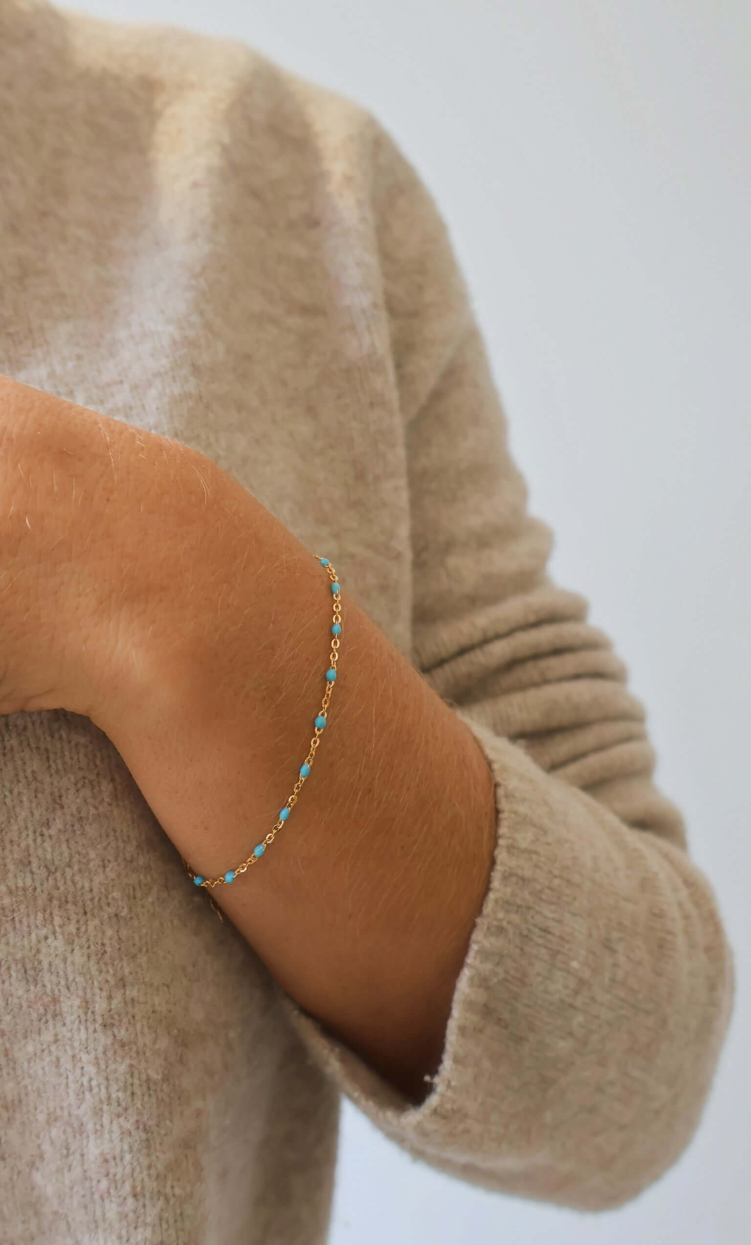 Close-up of a hand wearing a delicate 14k Gold Turquoise Beaded Bracelet on a beige sweater.