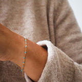 Close-up of a hand wearing a 14k gold turquoise beaded bracelet with a cozy sweater, showcasing ocean-inspired color.