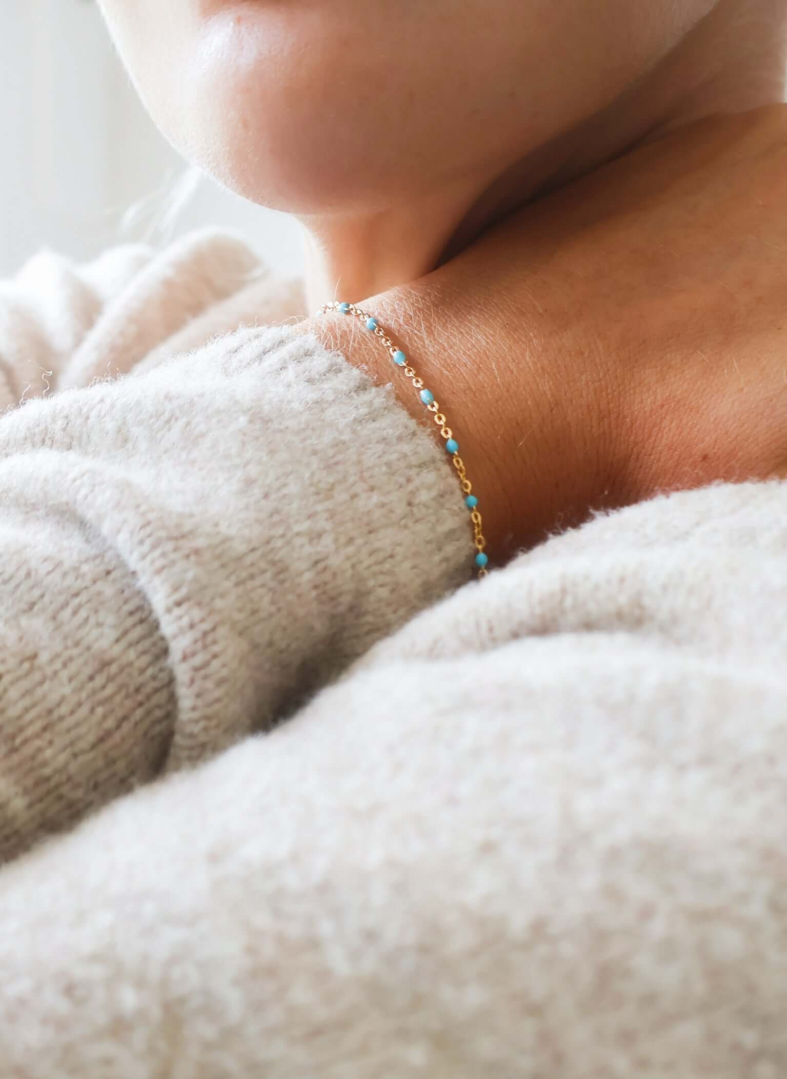 Close-up of a person wearing a 14k gold-filled turquoise beaded bracelet on a cozy sweater.