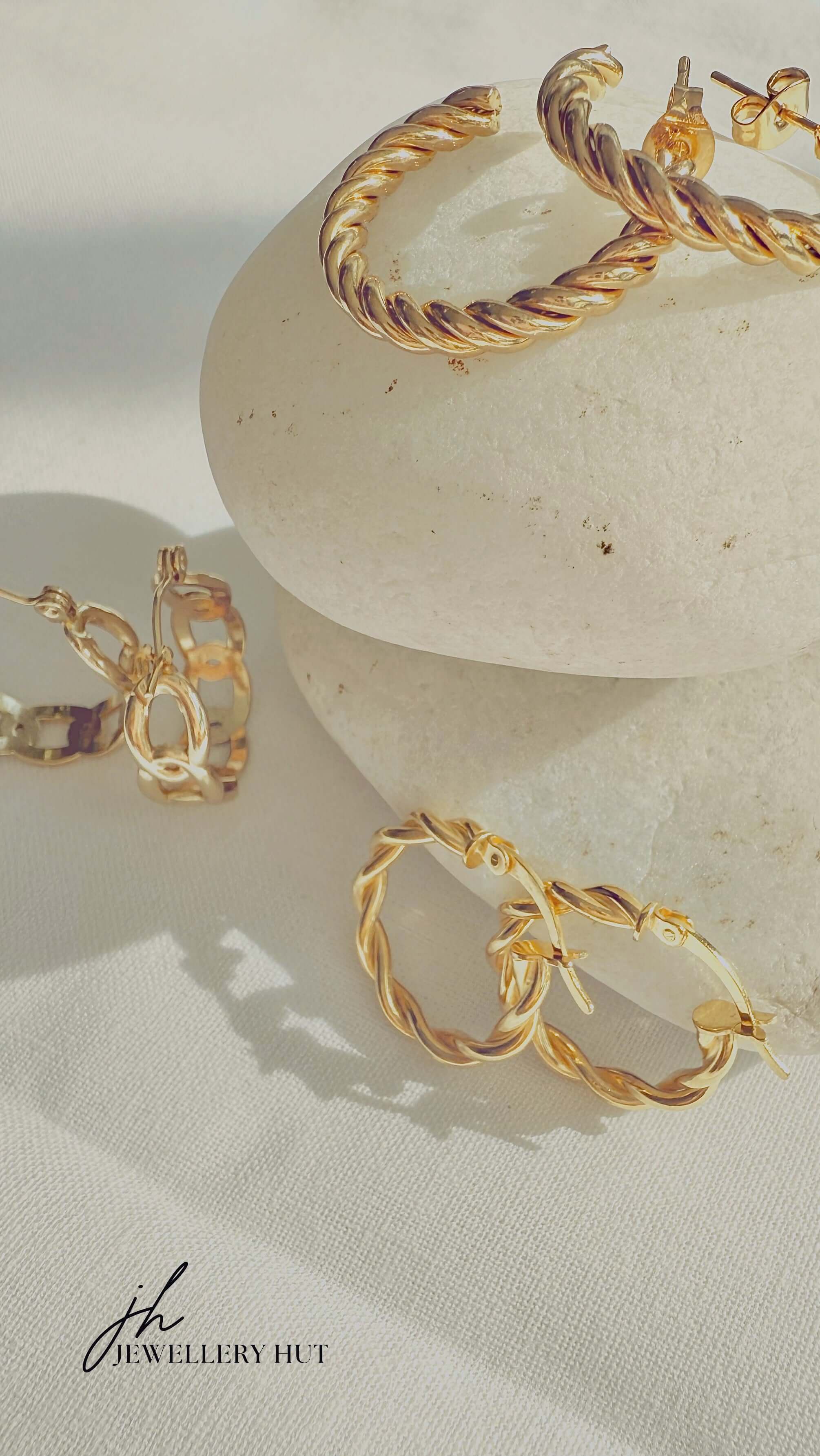 18k Gold Twisted Rope Hoop Earrings displayed elegantly on smooth stones, showcasing luxury and sophistication.