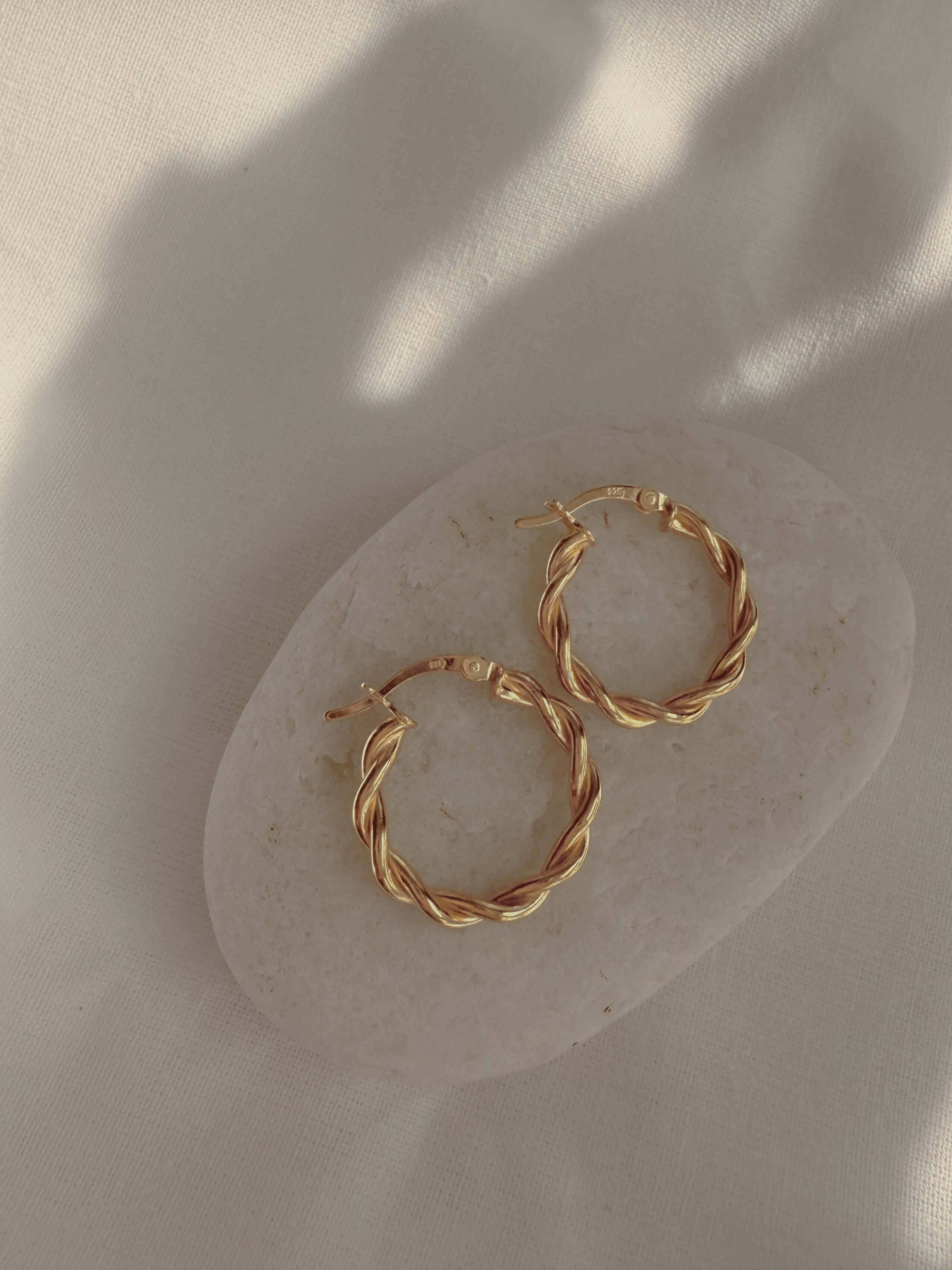 18k gold twisted rope hoop earrings on a neutral stone, showcasing elegance and sophistication in jewelry.