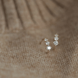 Tiny gold huggie half hoop earrings with three sparkling cubic zirconia stones, elegantly displayed on soft fabric.