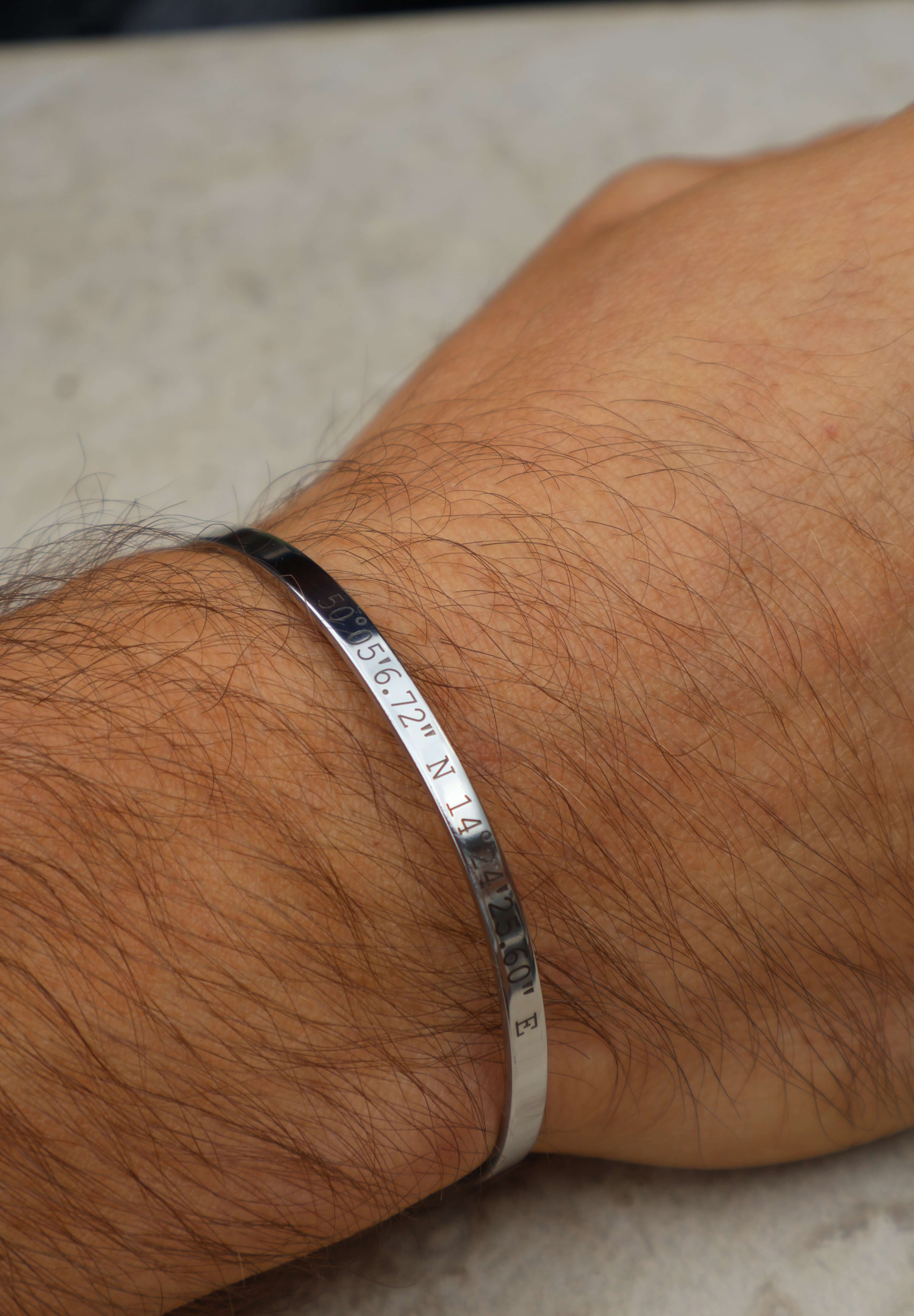 Personalised silver cuff bracelet with engraved coordinates worn on a wrist, showcasing a meaningful custom design.