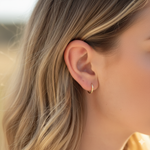 Close-up of a person wearing a gold hoop earring with blurred background
