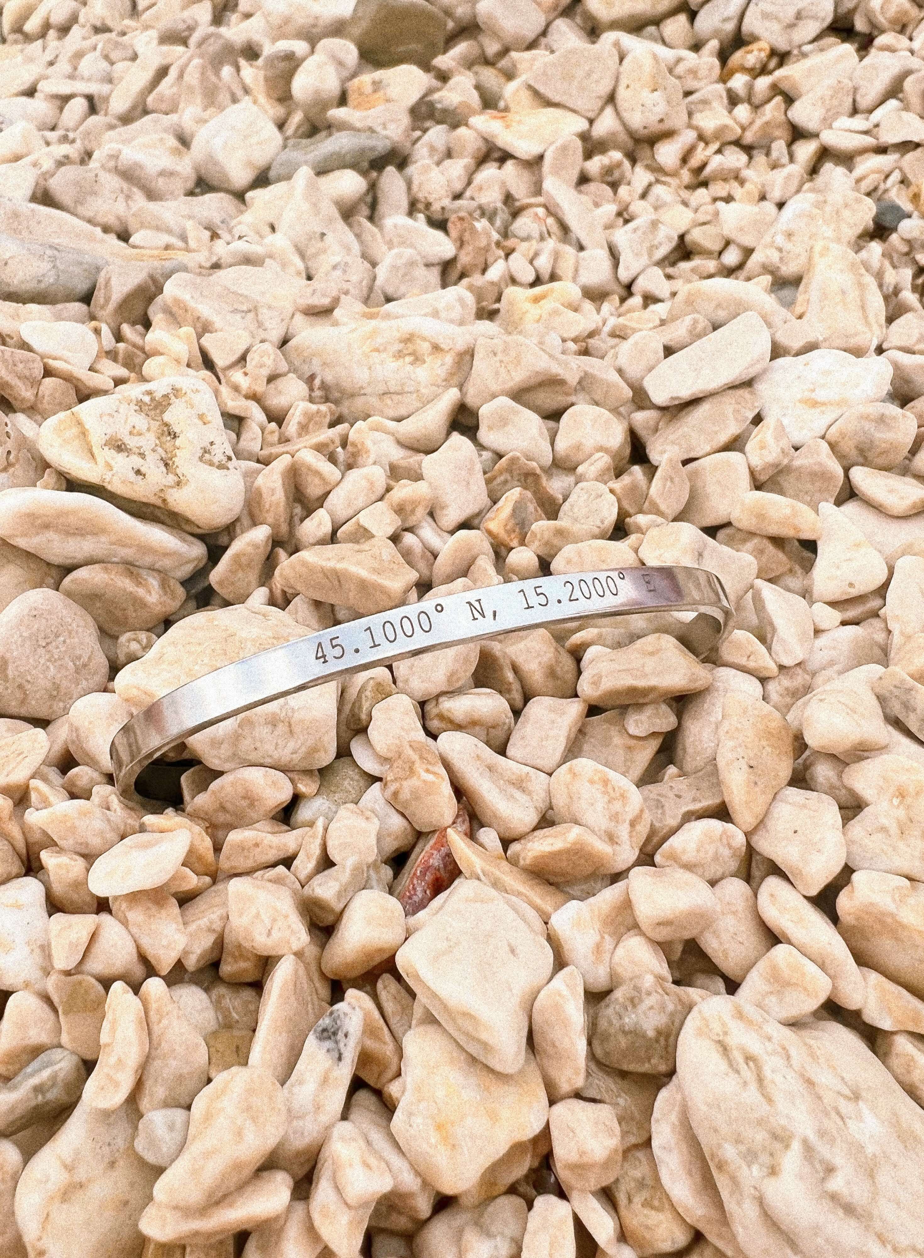 Personalised silver cuff bracelet with coordinates displayed on rocky surface for a meaningful gift.