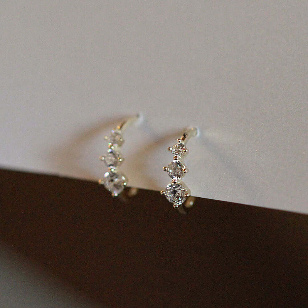 Tiny gold huggie half hoop earrings featuring three radiant cubic zirconia stones, elegantly displayed.