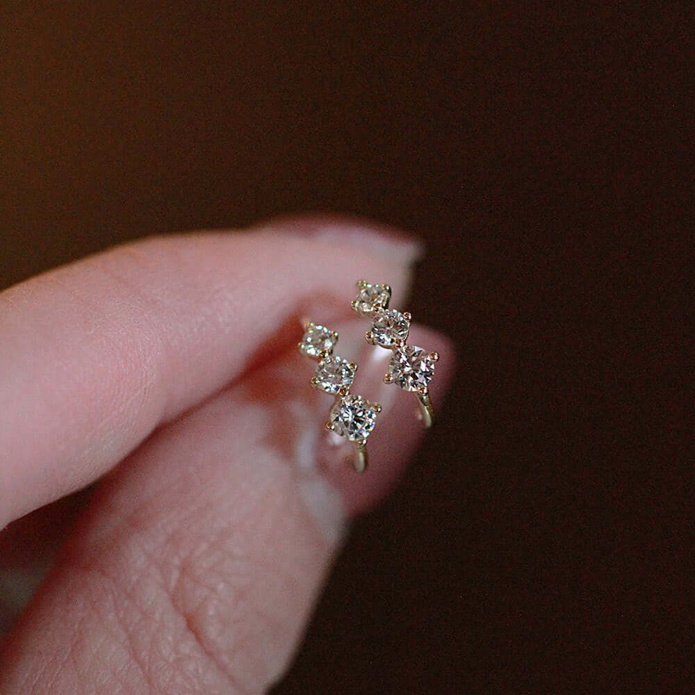 Tiny gold huggie half hoop earrings with cubic zirconia stones held between fingers.