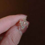 Tiny gold huggie half hoop earrings with cubic zirconia stones held between fingers.