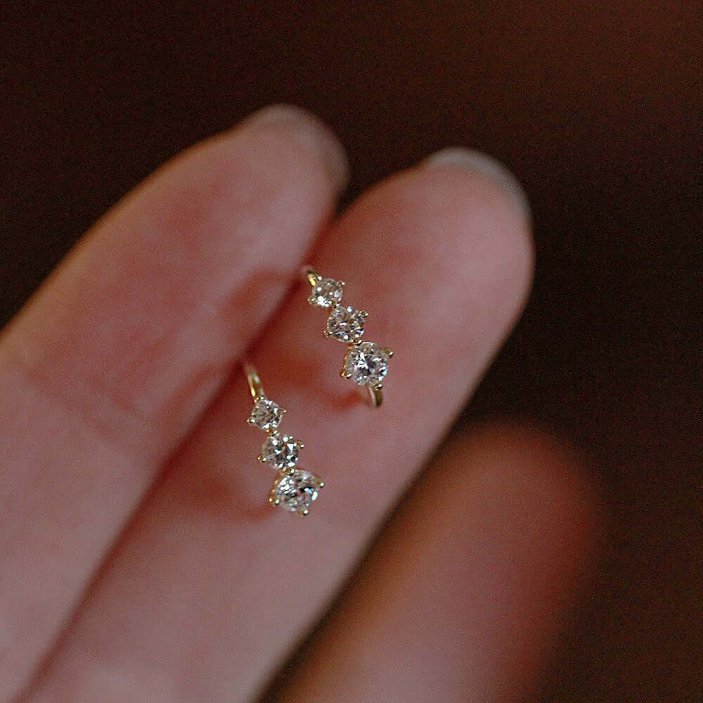 Tiny gold huggie half hoop earrings with three sparkling cubic zirconia stones in hand.
