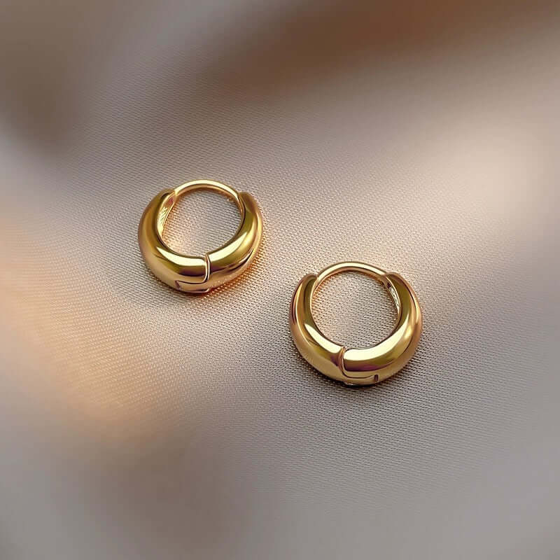 Gold oval hoop earrings showcasing timeless elegance and sophistication on a soft fabric backdrop.