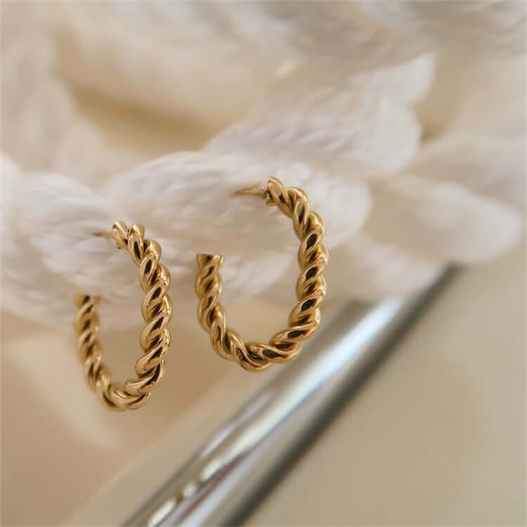 Twisted gold hoop earrings displayed on a textured background, perfect for stylish accessorizing.