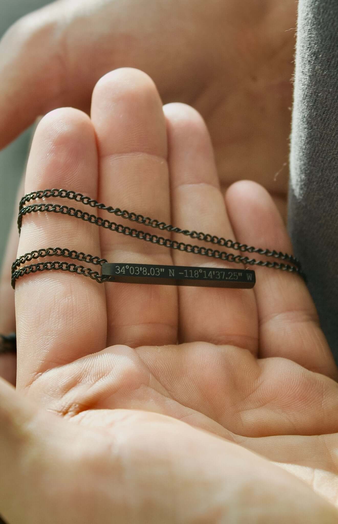 Black personalised bar necklace held in hand, featuring engraved coordinates for a meaningful gift.