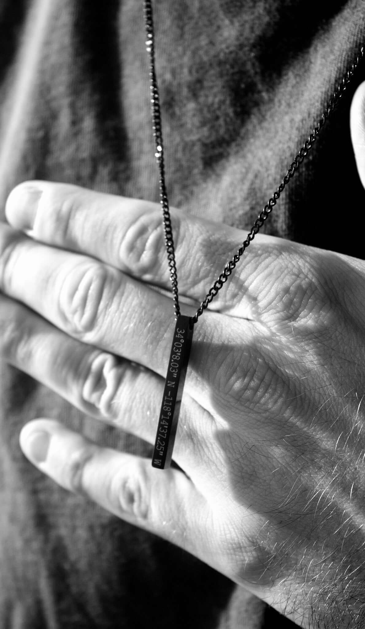 Close-up of a hand holding a black personalised bar necklace, showcasing its elegance and engraved design.