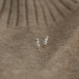 Tiny gold huggie half hoop earrings with cubic zirconia stones on a textured background.