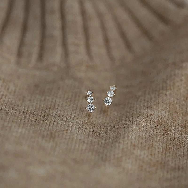Tiny gold huggie half hoop earrings with cubic zirconia stones on a textured background.