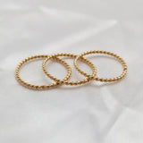 Three gold twisted stacking rings arranged elegantly on soft fabric.