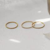 Three gold twisted stacking rings on a light background, showcasing versatile and elegant design.