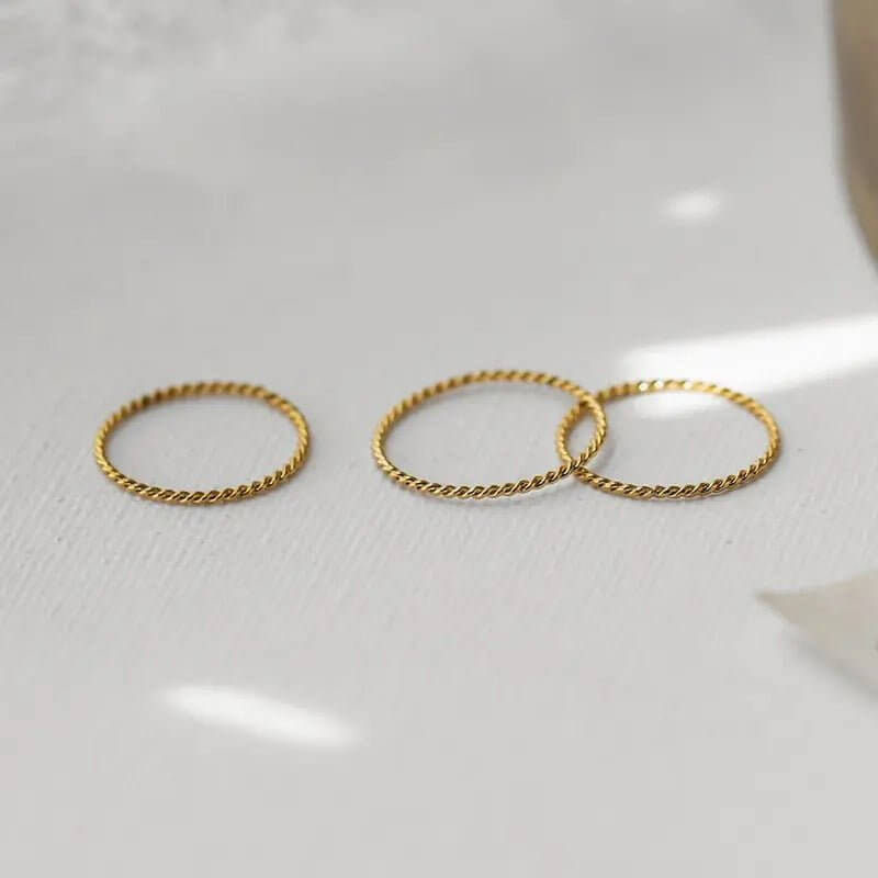 Three gold twisted stacking rings on a light background, showcasing versatile and elegant design.