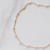 Gold satellite bracelet with sterling silver beads on a marble background.