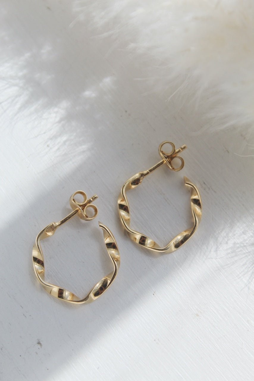 Gold twisted hoop earrings on a white surface, featuring a secure butterfly closure for comfort and style.