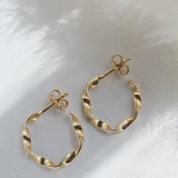 Gold twisted hoop earrings on a white surface, featuring a secure butterfly closure for comfort and style.