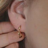 Gold twisted hoop earrings showcased on a model's ear, highlighting their elegant design and secure fit.