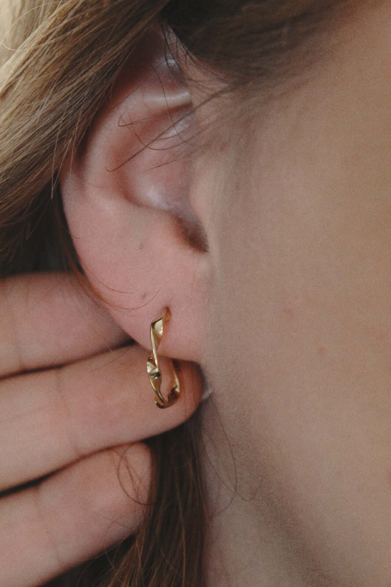 Gold twisted hoop earrings showcased on a model's ear, highlighting their elegant design and secure fit.