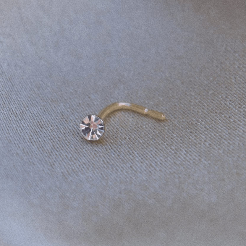 Gold nose ring with crystal detail on soft fabric background, perfect for every occasion.