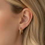 Close-up of a woman wearing a gold hoop earring with a neutral background