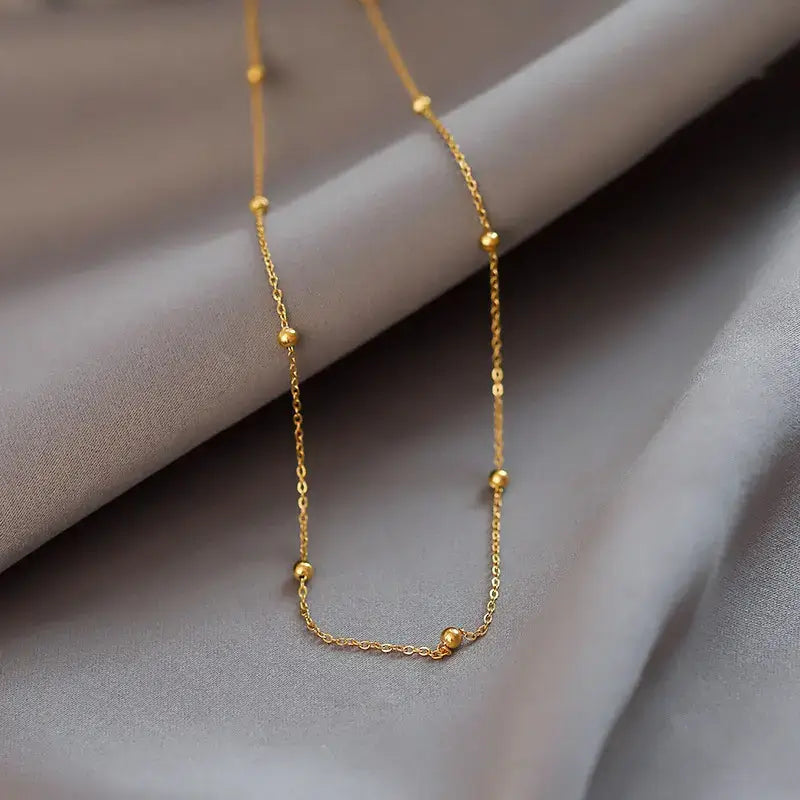 14K Gold Chunky Bead Necklace resting on soft gray fabric, showcasing its elegant design and quality craftsmanship.