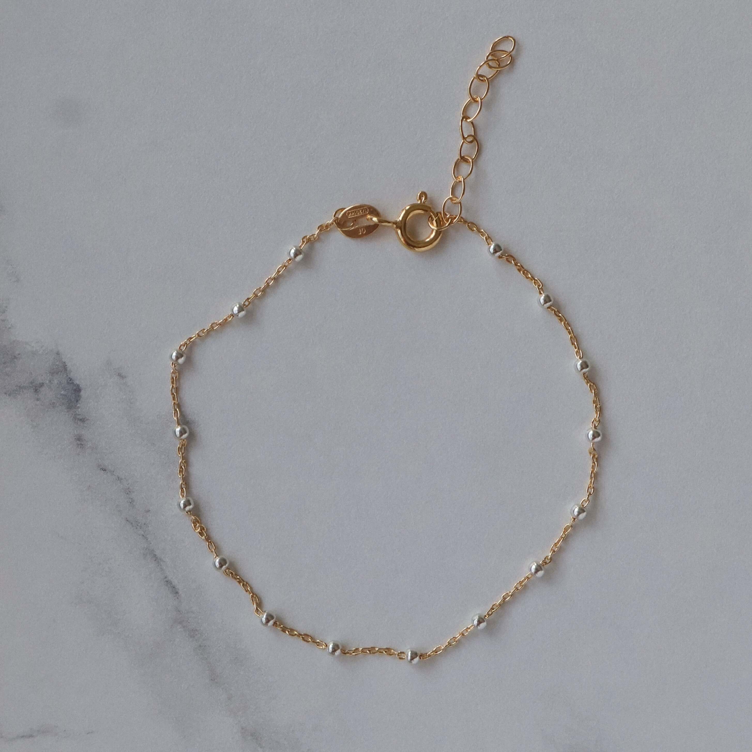 Silver Beaded 14k Gold Satellite Bracelet on marble background, adjustable for comfort and style.