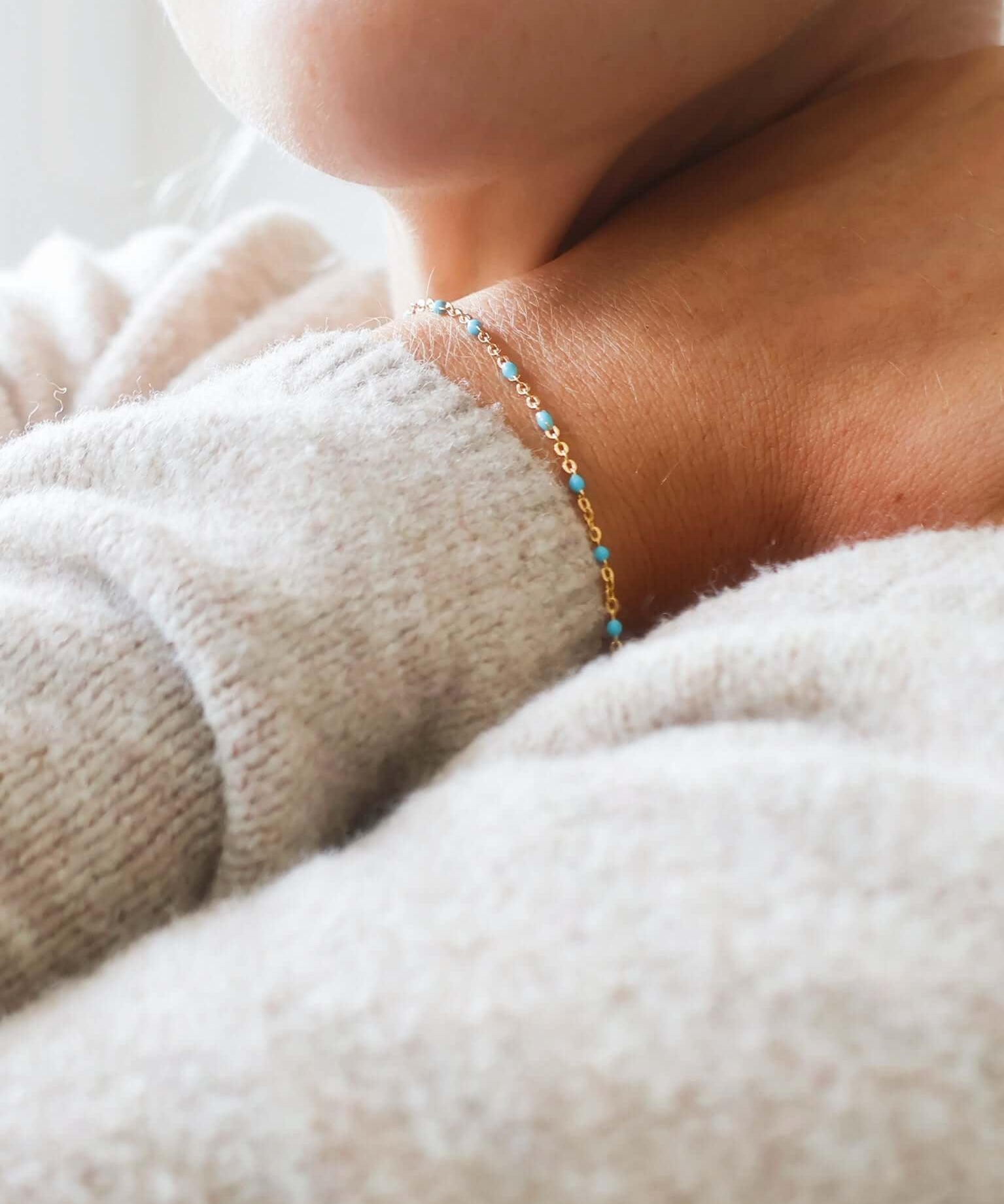Close-up of a person wearing a 14k gold-filled turquoise beaded bracelet on a cozy sweater.