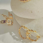 18k Gold Twisted Rope Hoop Earrings displayed elegantly on smooth stones, showcasing luxury and sophistication.