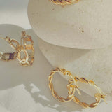 18k Gold Twisted Rope Hoop Earrings displayed elegantly on smooth stones, showcasing luxury and sophistication.