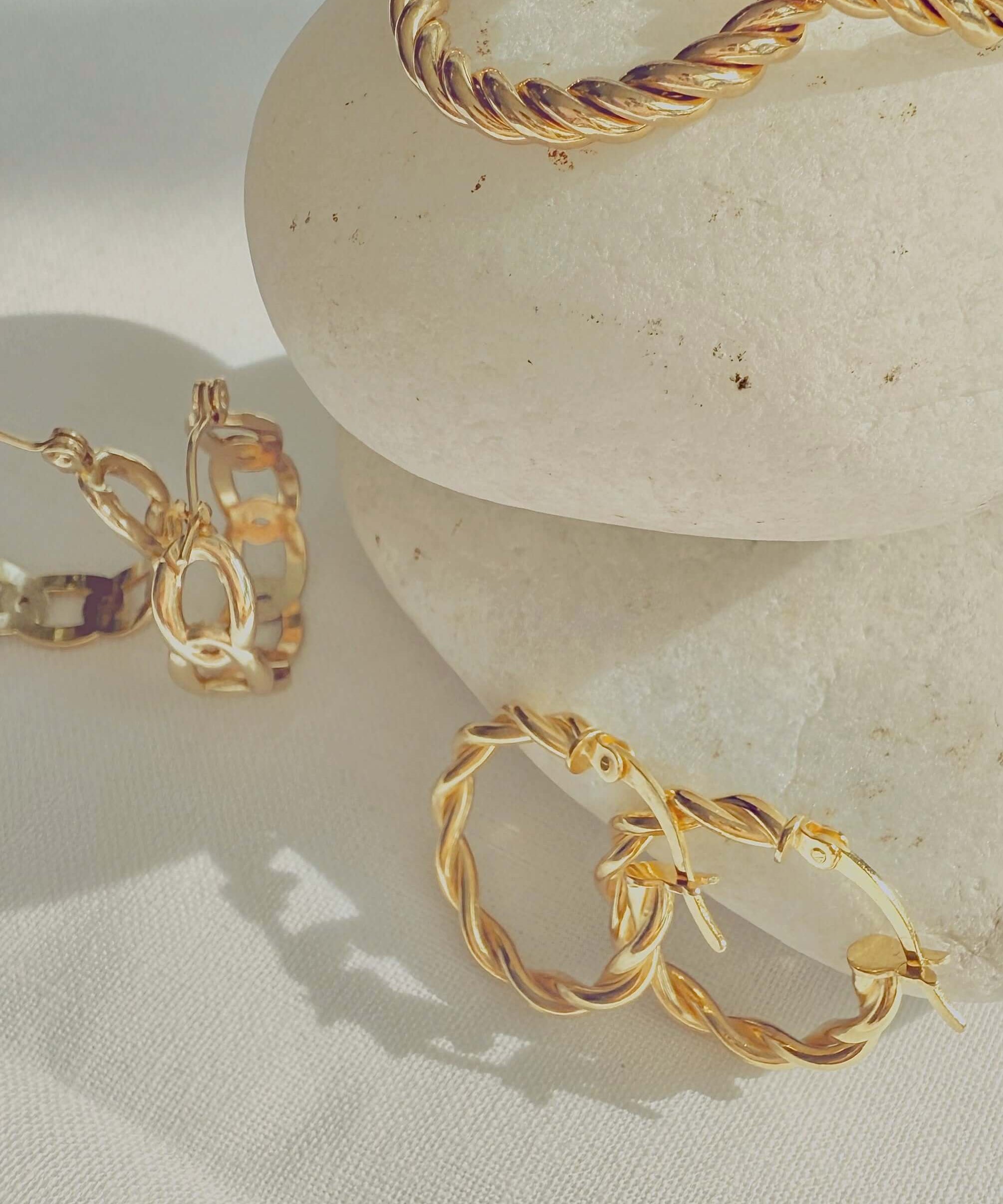 18k Gold Twisted Rope Hoop Earrings displayed elegantly on smooth stones, showcasing luxury and sophistication.