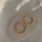 18k gold twisted rope hoop earrings on a neutral stone, showcasing elegance and sophistication in jewelry.