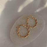 18k gold twisted rope hoop earrings on a neutral stone, showcasing elegance and sophistication in jewelry.