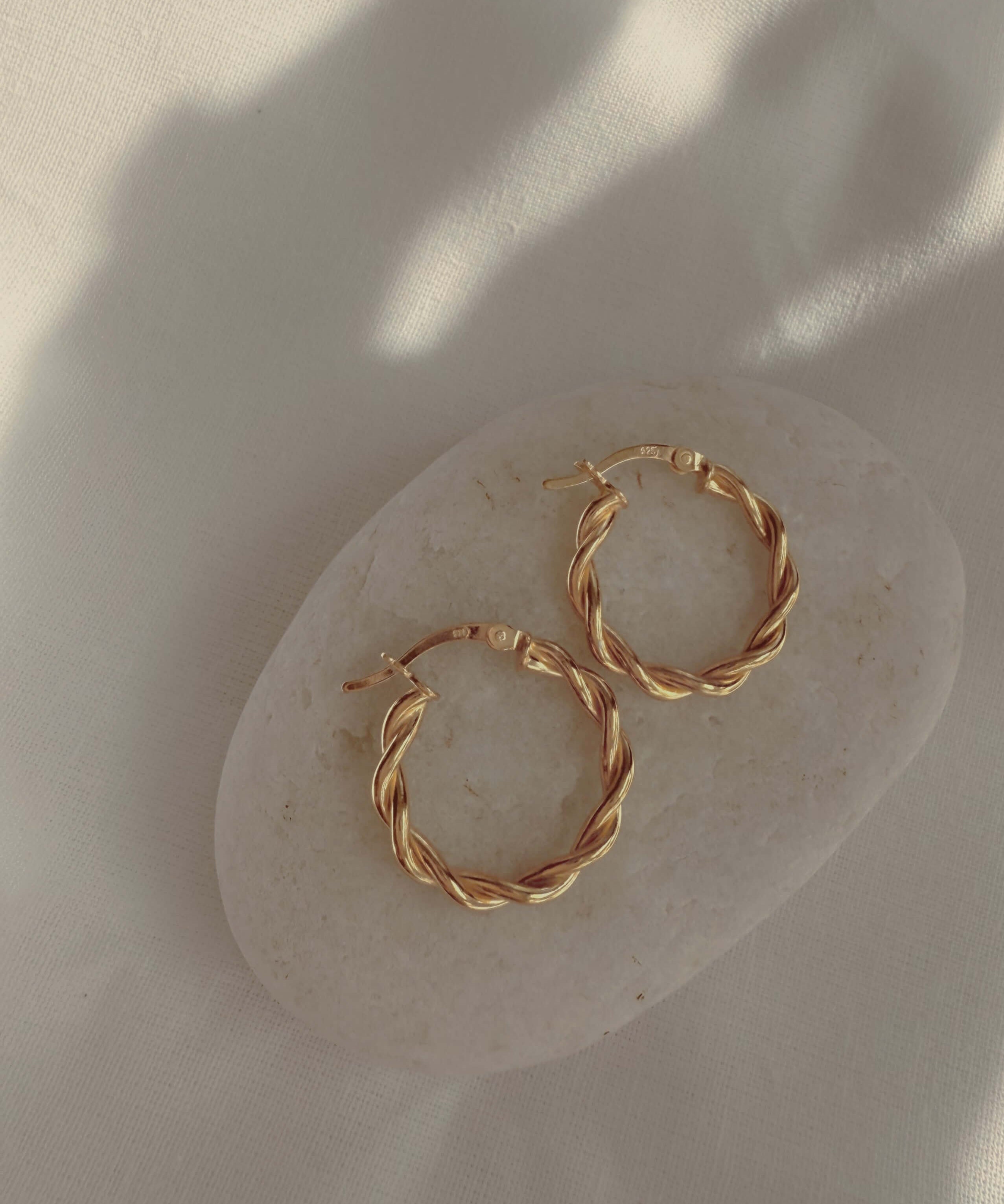 18k gold twisted rope hoop earrings on a neutral stone, showcasing elegance and sophistication in jewelry.
