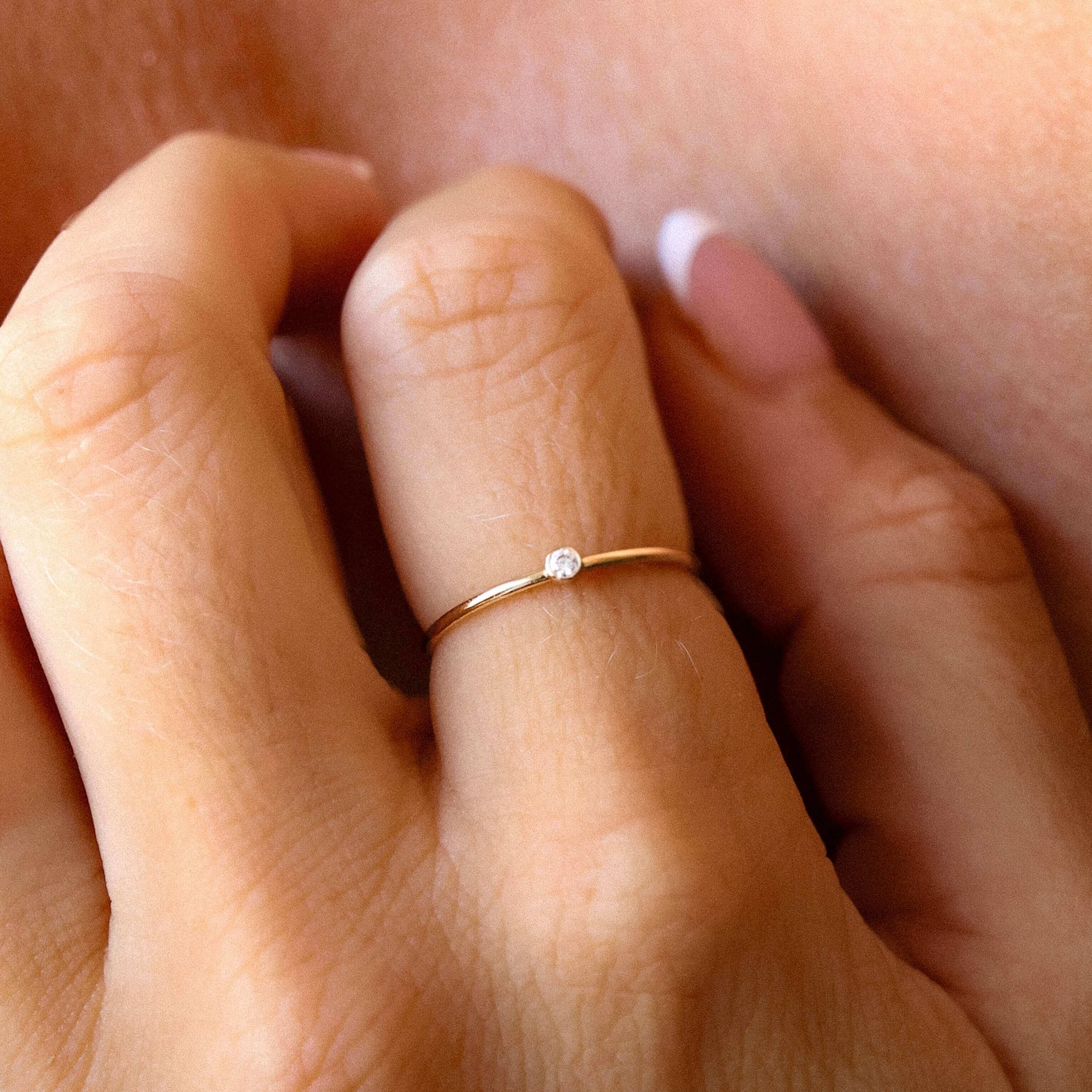 Close-up of a hand wearing a gold ring with a small diamond on a soft background