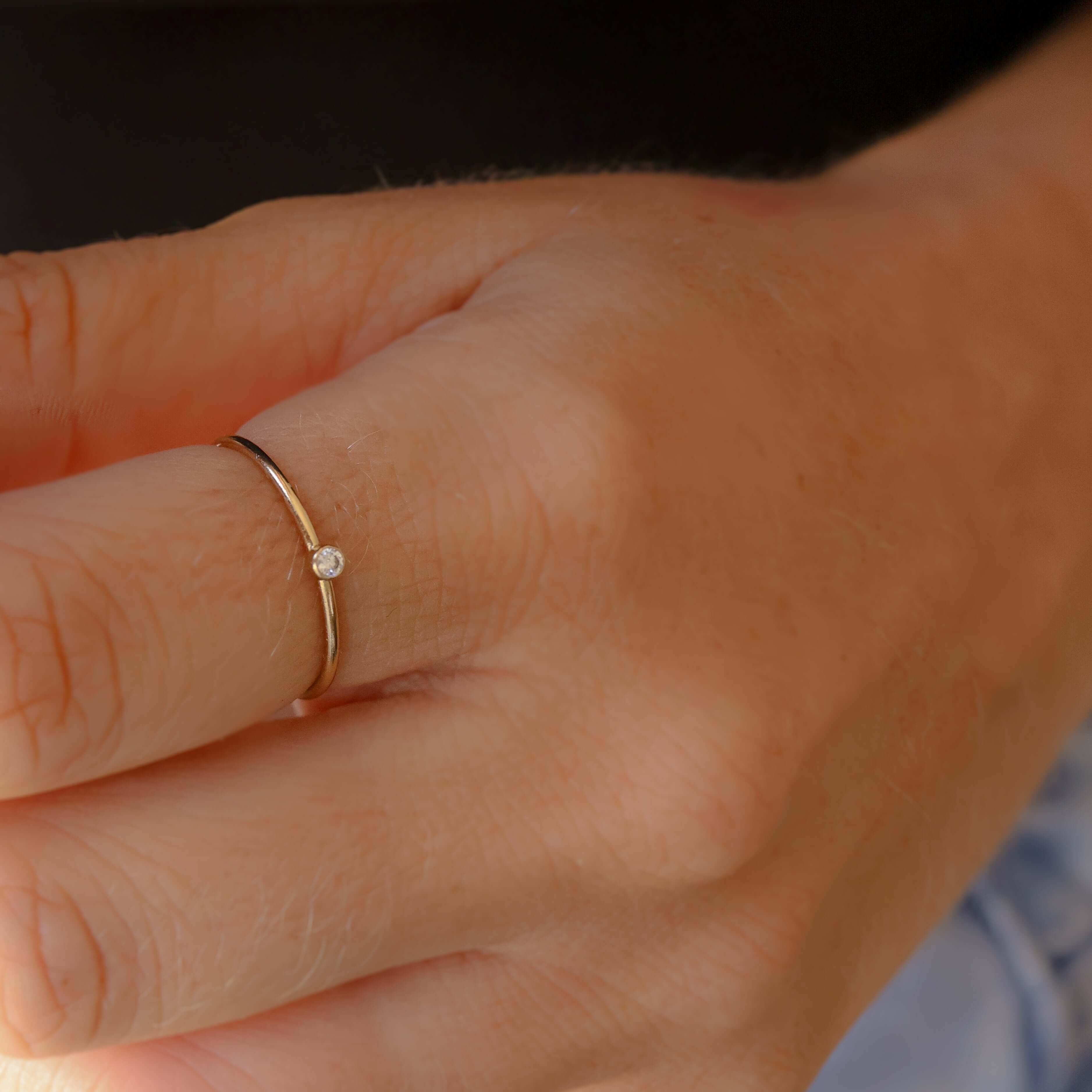 Close-up of a hand wearing a gold ring with a small diamond on a blurred background