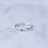 Silver ring with a single letter 'K' on a marble surface