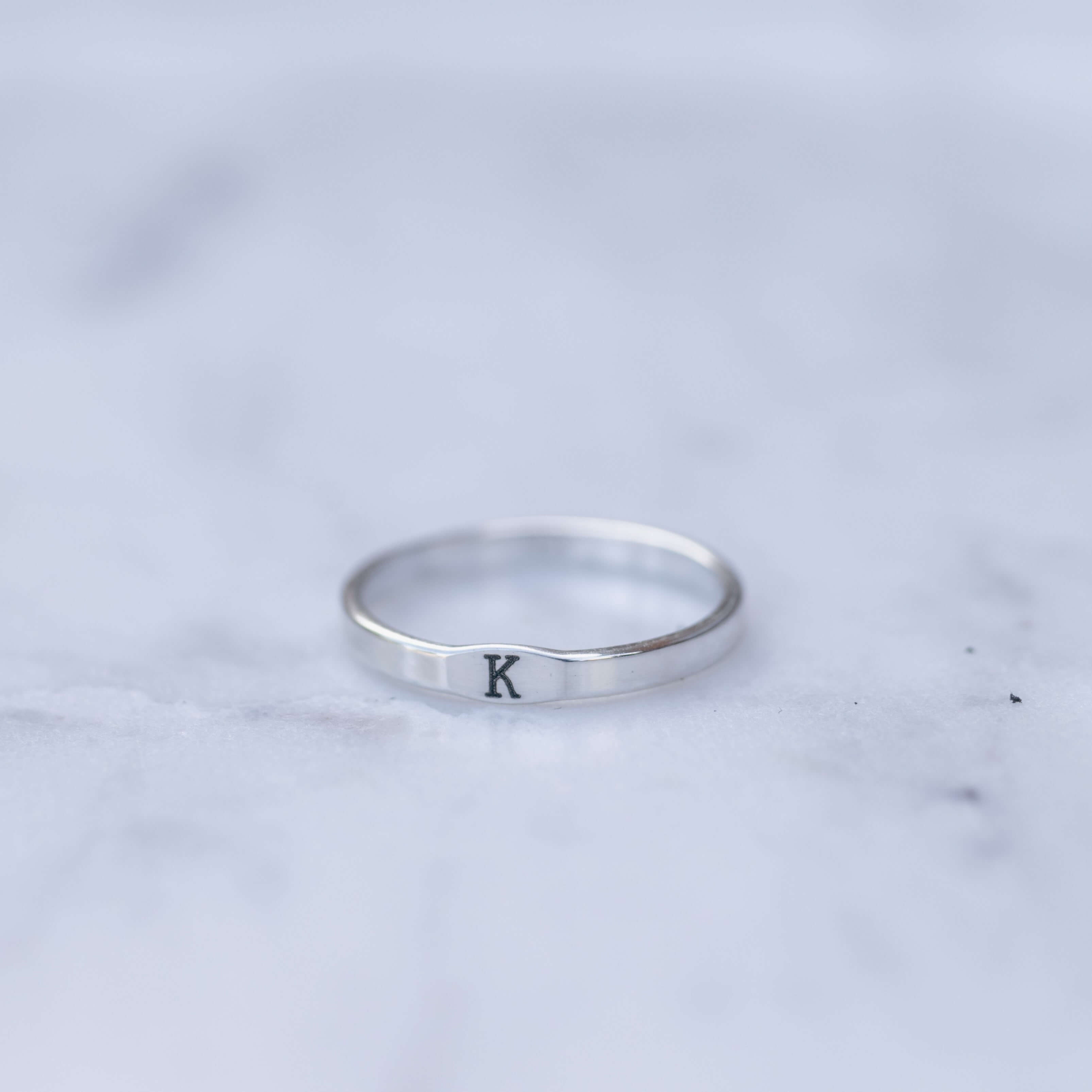 Silver ring with a single letter 'K' on a marble surface