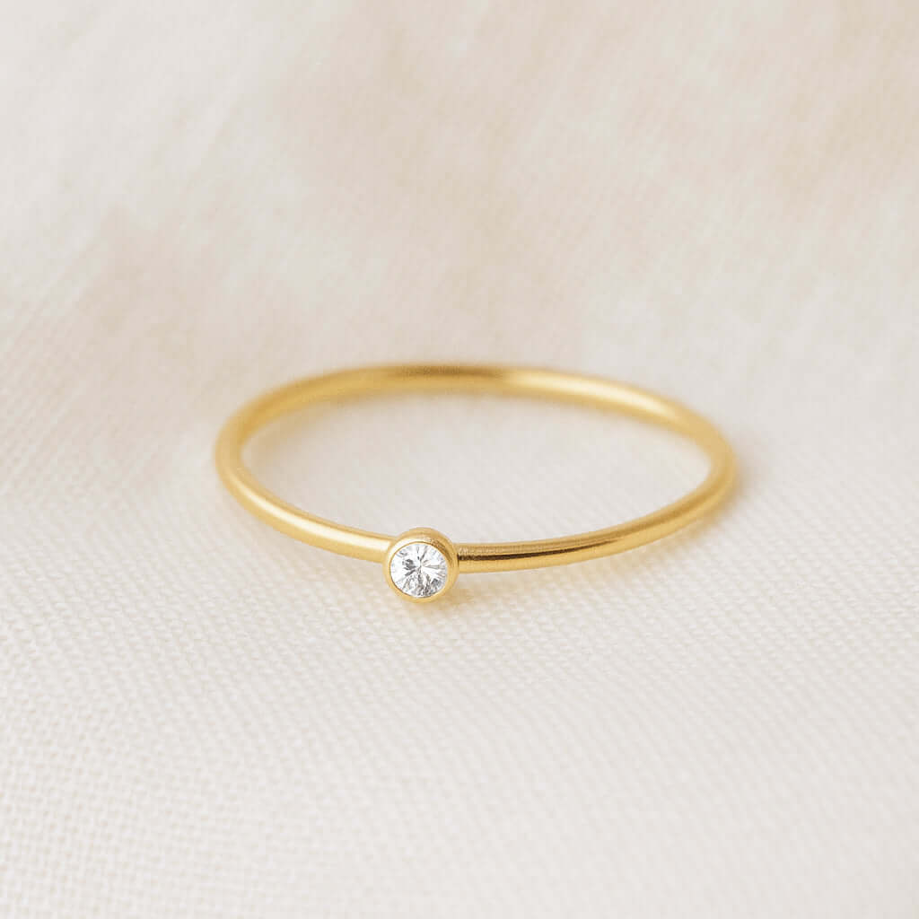 Gold ring with a small diamond on a beige fabric background