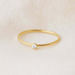 Gold ring with a small diamond on a beige fabric background