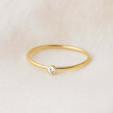Gold ring with a small diamond on a beige fabric background