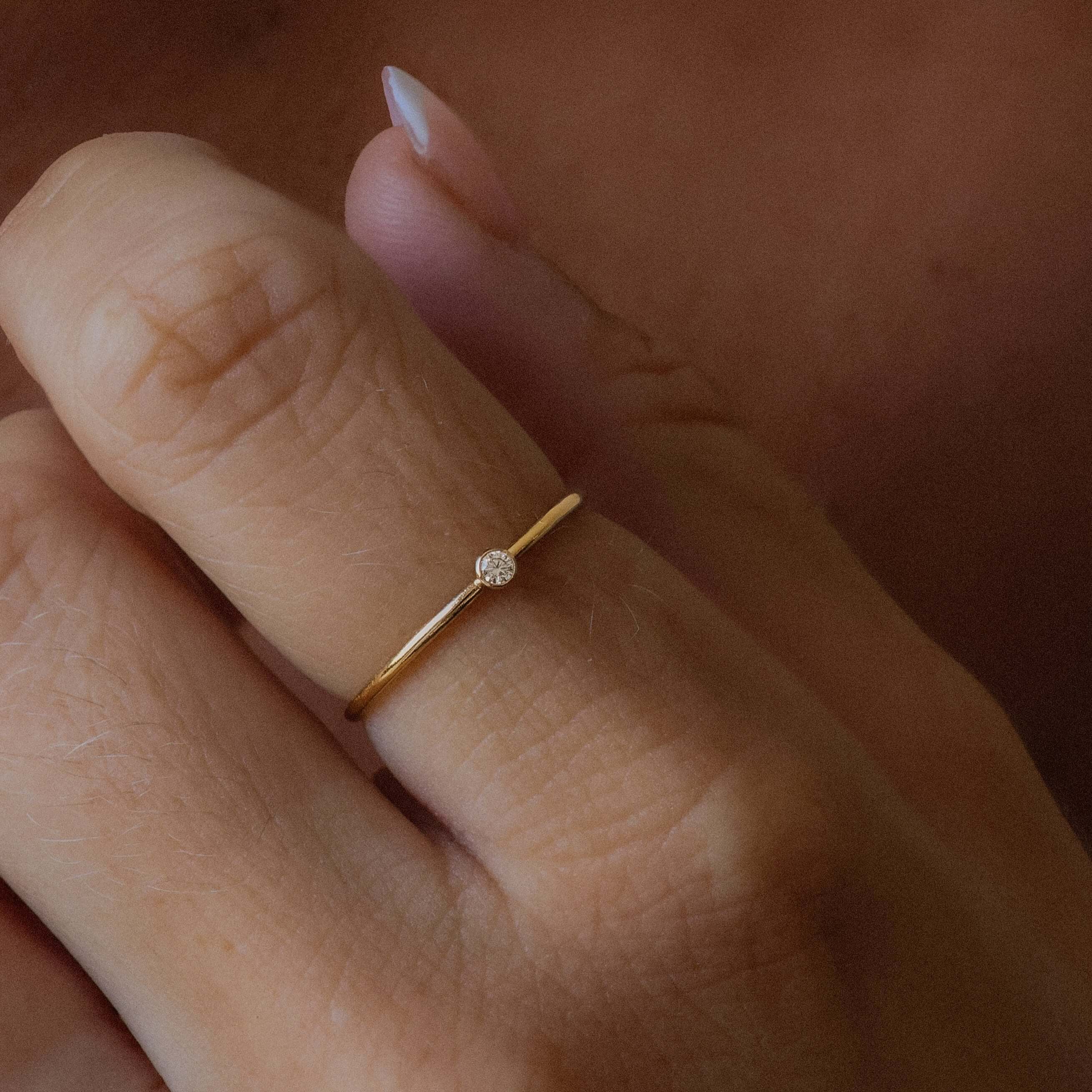 Gold ring with a small diamond on a person's finger against a neutral background