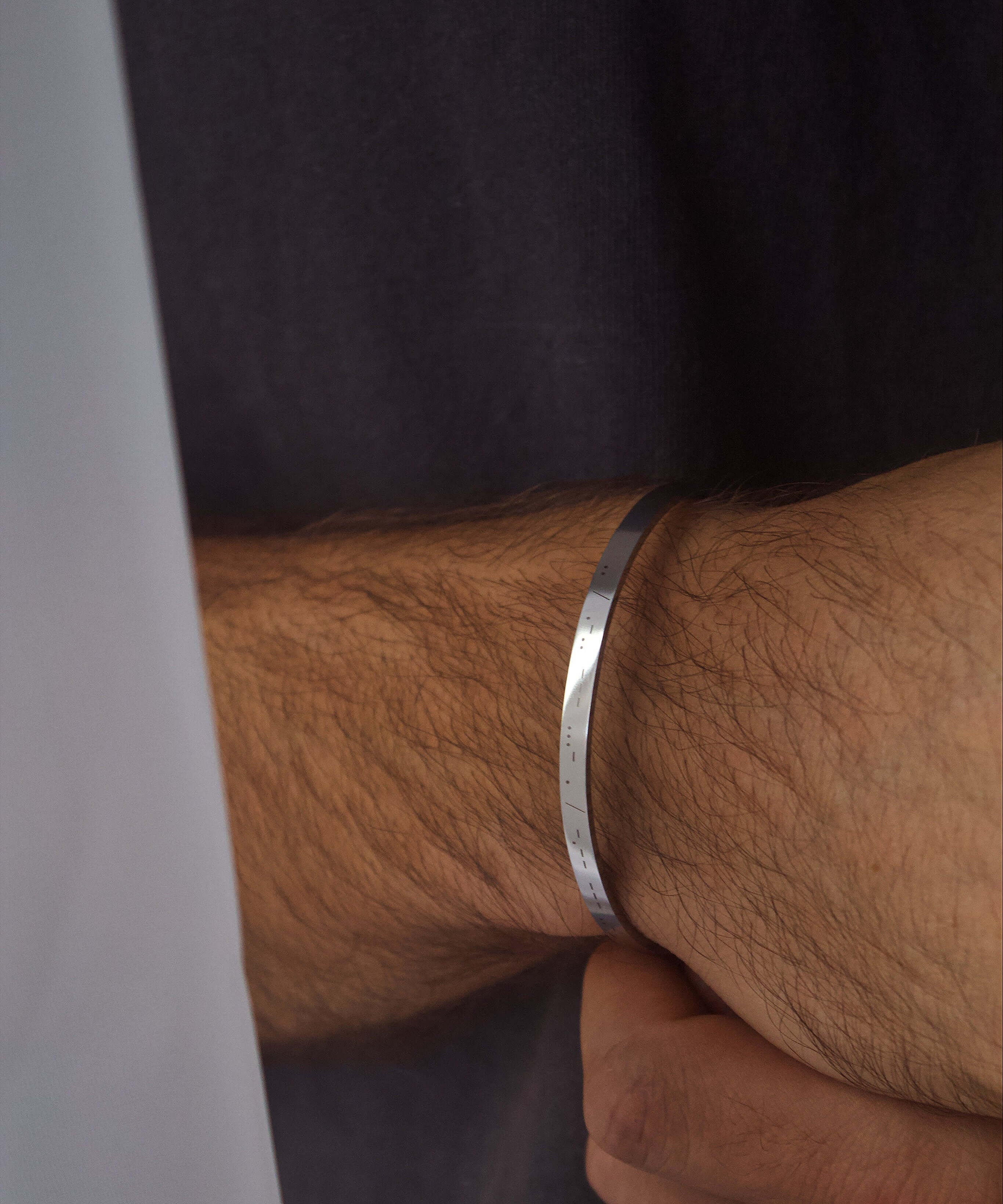 Stylish silver personalised cuff bracelet worn on a man's wrist, featuring custom engraving for added meaning.