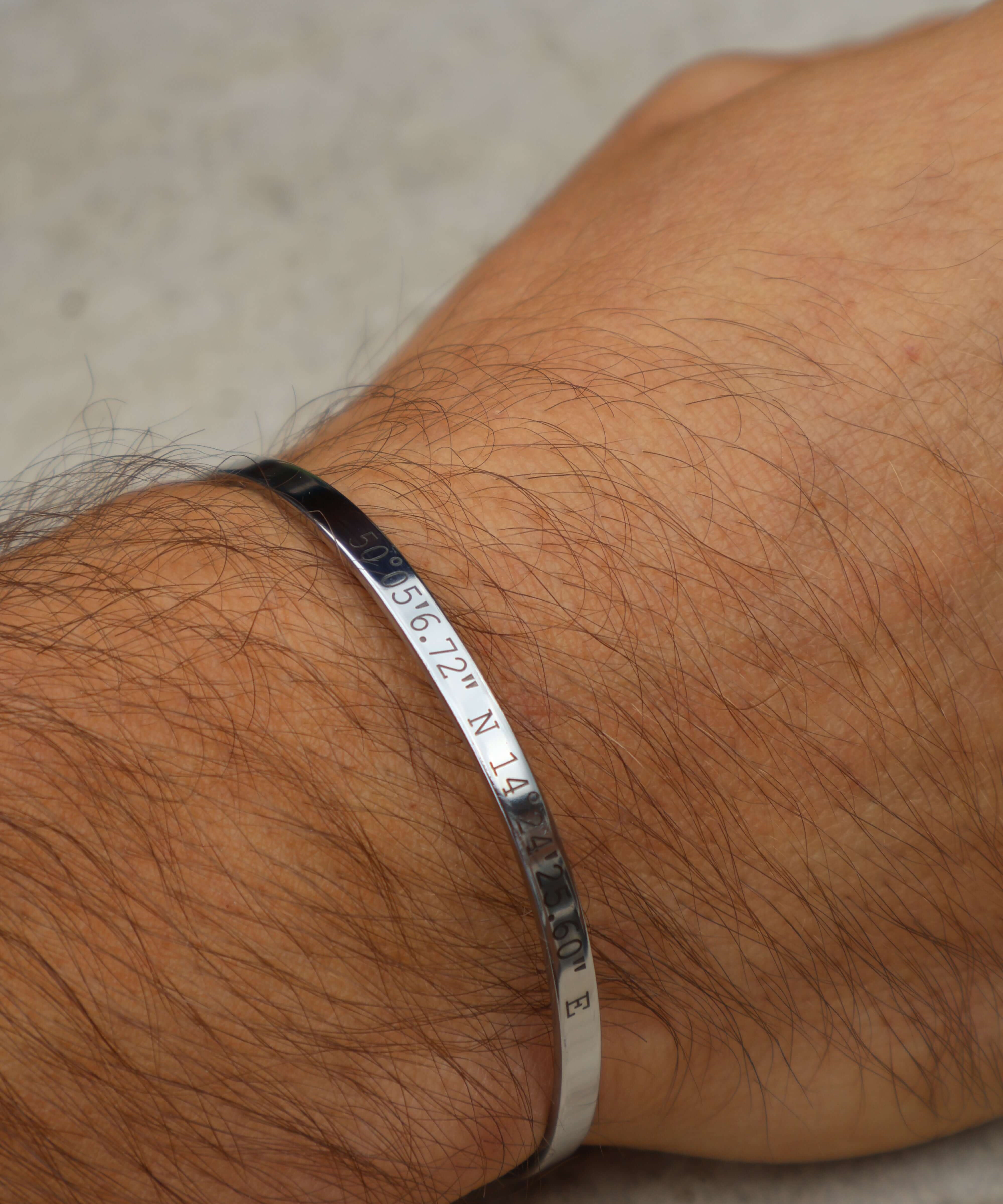 Personalised silver cuff bracelet with engraved coordinates worn on a wrist, showcasing a meaningful custom design.