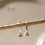 Silver earrings on a wooden stick against a beige background